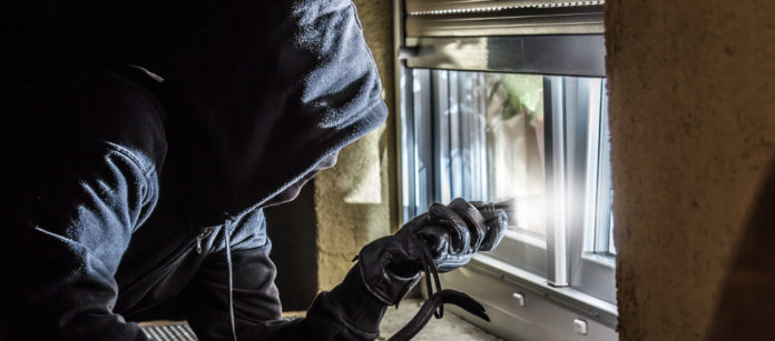 rapinatore con passamontagna davanti a finestra con piede di porco