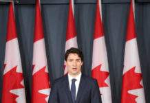 Il governo canadese fa sul serio sul divieto di detenzione di armi d’assalto e pistole Il primo ministro canadese Justin Trudeau dietro a un podio davanti a nove bandiere canadesi. Si va verso il divieto di detenzione di armi d'assalto e di pistole.