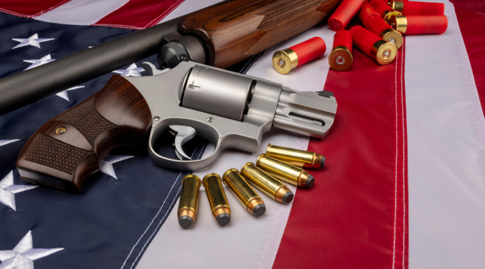 Background check richiesti in America, il dato finale del 2021 Background check richiesti in America: revolver e fucile con munizioni su bandiera americana