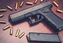Scadenza del porto d’armi e stato d’emergenza: che succede? Scadenza del porto d’armi e stato d'emergenza: pistola Glock su tavolo di legno con munizioni